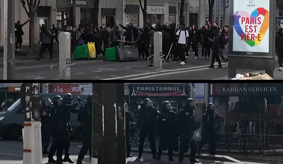 Un grup de persoane stă pe un drum urban lângă containere de deșeuri, în timp ce figuri în uniformă întunecată stau pe trotuar.