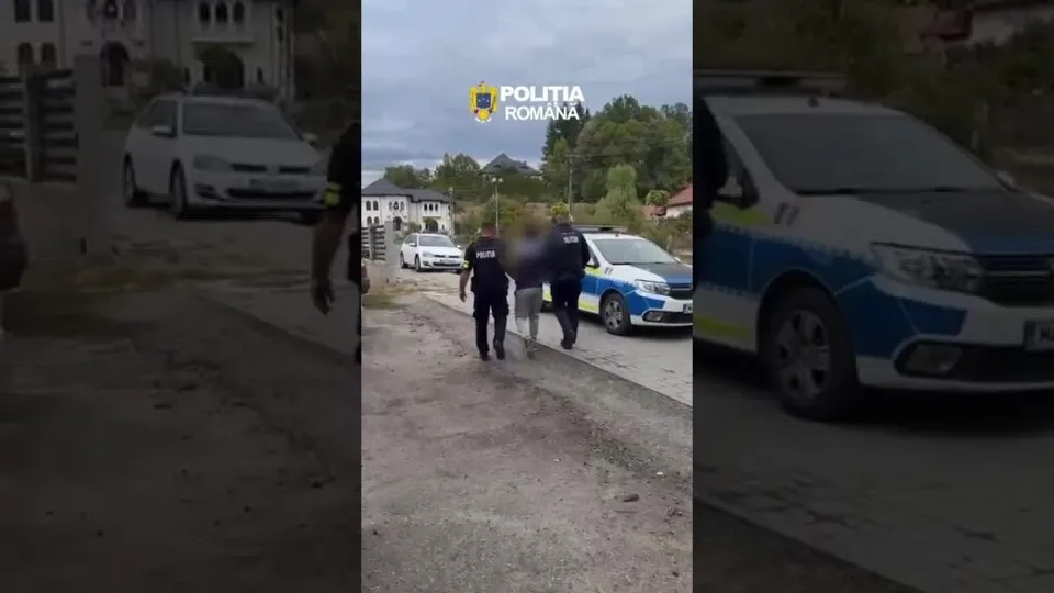 Trei persoane în uniformă întunecată stau lângă două mașini de poliție parcate pe un drum de pietriș lângă o clădire.