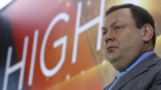 Un bărbat cu părul scurt și haine de business este surprins într-o poziție laterală în fața unui fundal cu litere mari albe.