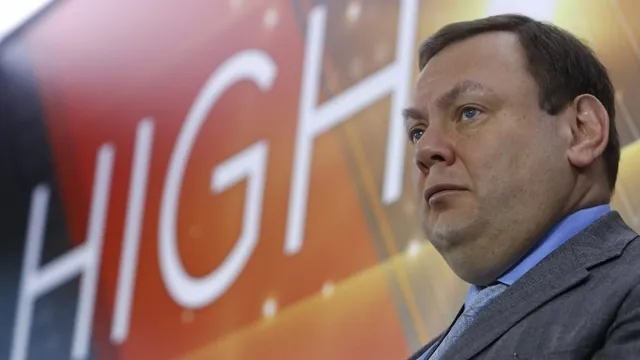 Un bărbat cu părul scurt și haine de business este surprins într-o poziție laterală în fața unui fundal cu litere mari albe.