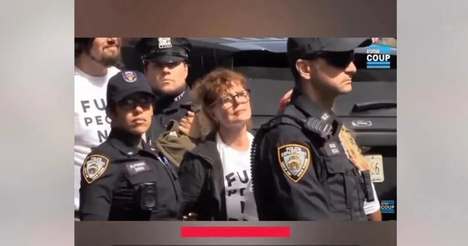 Un grup de polițiști în uniformă neagră stă lângă o femeie cu ochelari și tricou alb într-un spațiu exterior cu un vehicul în fundal.