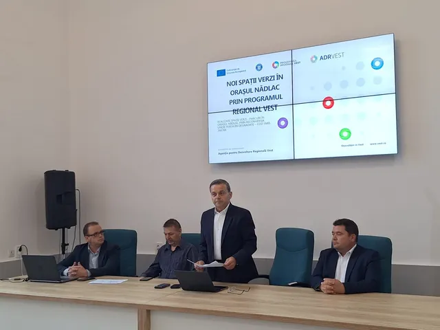 Patru bărbați stau la o masă lungă de lemn în fața unui ecran mare care afișează un text și câteva logo-uri.