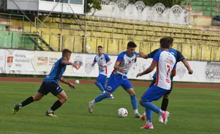 Cinci jucători de fotbal de pe un teren de gazon verde participă la un meci, având o minge albă pe iarbă.