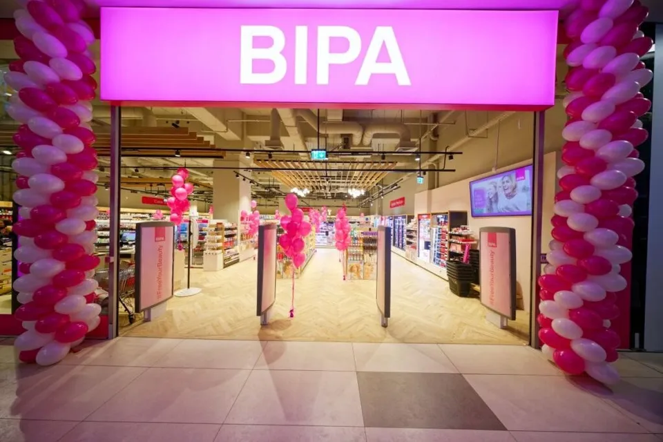 O intrare de magazin BIPA cu un panou roz luminoas cu denumirea, flanked de coloane de baloane roz și albe, cu interiorul luminos și produse vizibile.