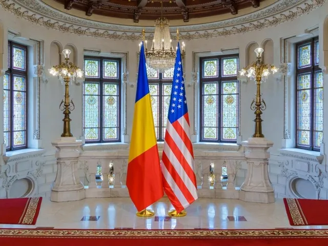 Două steaguri, unul galben, albastru și roșu și unul cu stele și dungi, sunt expuse într-o încăpere cu ferestre înalte și candelabre dorice.