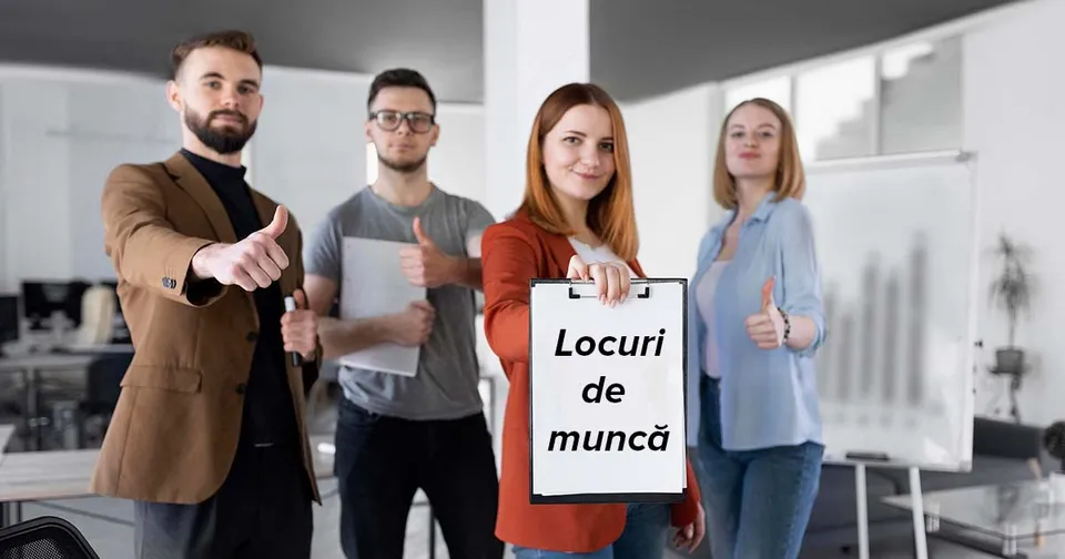 Patru persoane stau în rând într-un birou, două dintre ele făcând gestul cu degetul mare și o femeie ținând un dosar alb.