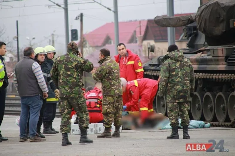 Oameni în uniforme militare de camuflaj și salvatori în haine roșii stau lângă un vehicul blindat pe o suprafață asfaltată.
