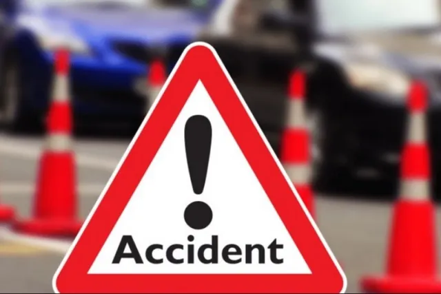 Un semn de circulație triunghiular cu margini roșii și un semn exclamării negru pe fundal alb este plasat în fața unor conuri de trafic și mașini.