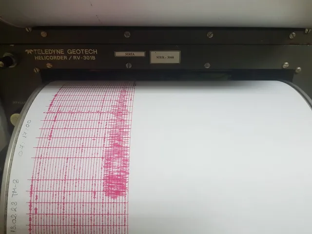 O imprimare de linii roz pe un cilindru de hârtie albă este vizibilă într-un aparat de înregistrare seismică.