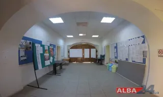 O cameră cu pereți albi conține panouri de afișaj cu diverse hârtii, un birou negru și câteva coșuri de gunoi colorate pe podea.