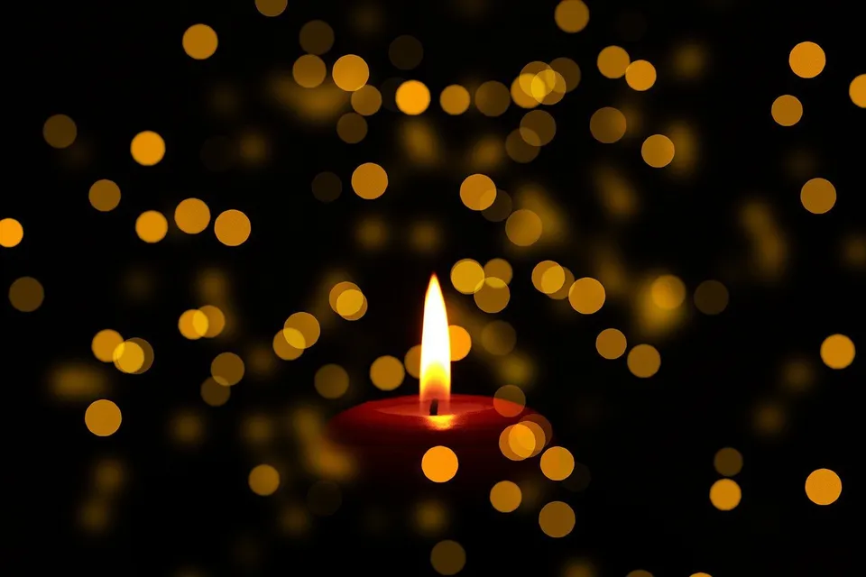 O lumânare aprinsă, roșie, pe un fundal negru cu luminițe bokeh aurii.