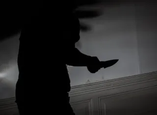 Silueta unei persoane întinse care ține un obiect tăietor în mână în fața unui perete deschis la culoare.