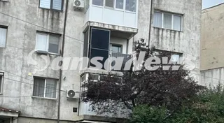 Panouri fotovoltaice negre sunt montate pe balconul unui apartament de la un etaj al unei clădiri gri cu ferestre și un arbore în prim-plan.