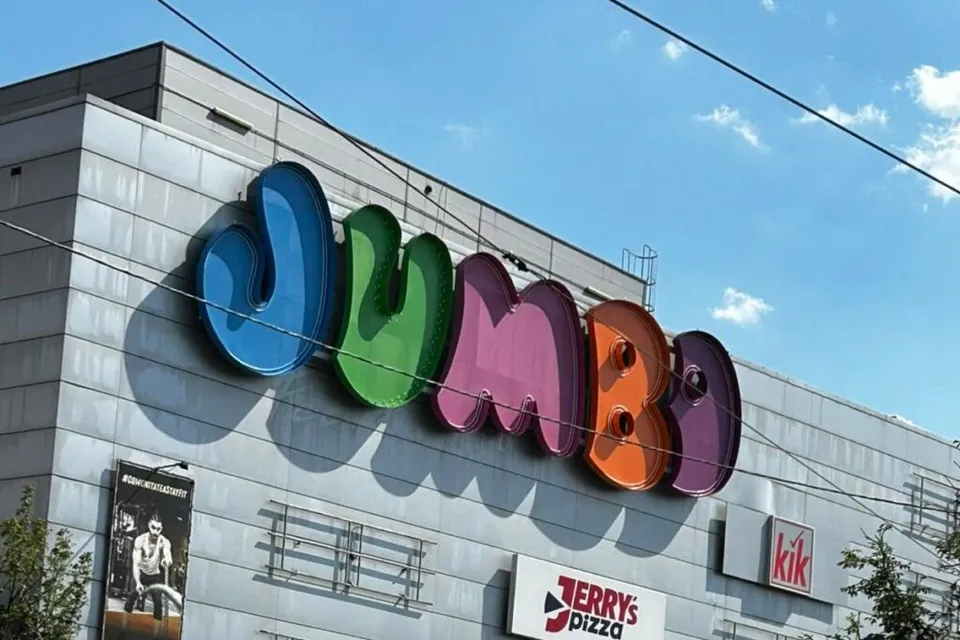 Un semn colorat cu litere mari este montat pe fațada unei clădiri gri sub un cer albastru.