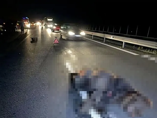 Un autoturism gri stă pe o șosea noapte, lângă un triunghi reflectorizant, în timp ce un obiect neclar și pixelat se află pe asfalt în prim-plan.