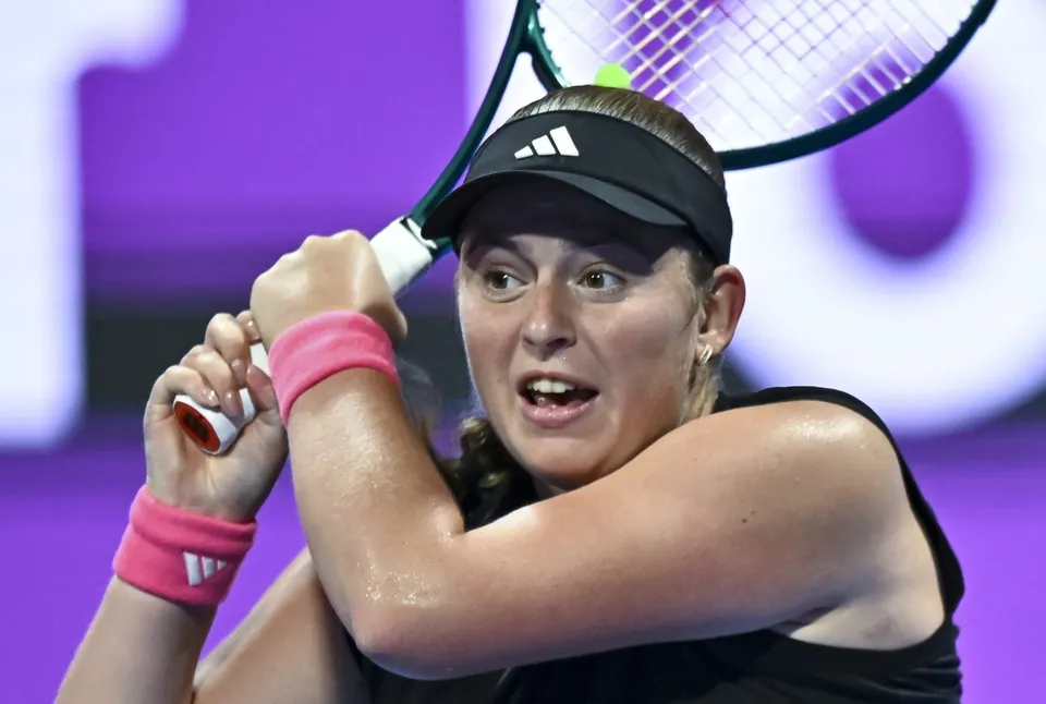 O femeie cu o șapcă neagră și brățări roz de mână ține o rachetă de tenis în poziție de lovitură.