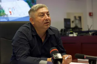 Un bărbat cu părul scurt și cămașă închisă stă la o masă în fața mai multor microfoane.