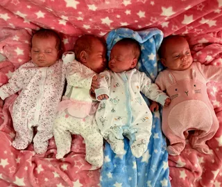 Patru nou-născuți îmbrăcați în pijama de culcare stau întinși pe o pătură roz cu motive stelare.