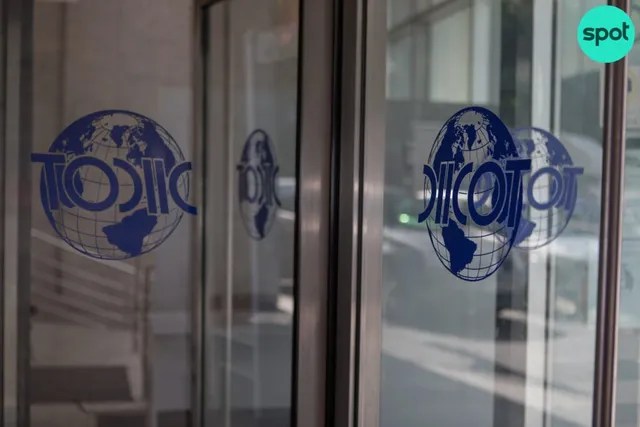 Un logo albastru reprezentând un glob terestru cu textul DIICOT este aplicat pe o suprafață de sticlă transparentă.