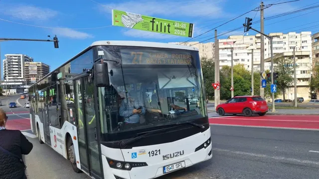 Un autobuz alb de tip Isuzu circulă pe un drum asfaltat lângă o pistă marcată cu roșu, sub un cer senin.