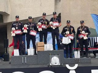 Cinci bărbați în uniforme de serviciu negre stau pe un podium de premiere ținând trofee, medalii și ursuleți de pluș.