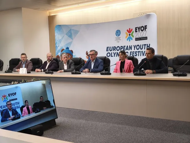 O scenă de conferință cu un panou de fundal EYOF și mai mulți oficiali așezați la o masă lungă, cu un monitor în prim plan afișând transmisia.