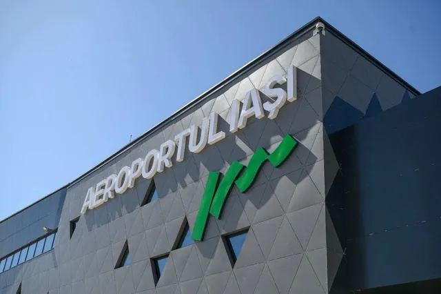 Scrisul alb AEROPORTUL IAȘI este montat pe fațada gri a unei clădiri sub un cer senin.