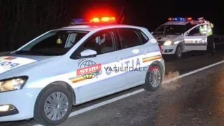 Două mașini de poliție albe cu girofare aprinse sunt parcate pe marginea unui drum asfaltat pe timp de noapte.