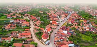 O vedere aeriană a unei localități cu case cu acoperișuri roșii, drumuri și zone verzi întinse.