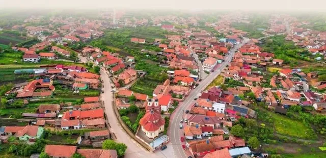 O vedere aeriană a unei localități cu case cu acoperișuri roșii, drumuri și zone verzi întinse.