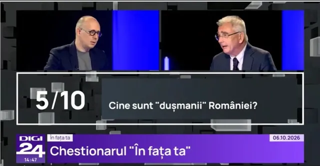 Un bărbat cu ochelari și bluie neagră stă lângă un alt bărbat cu ochelari, cămașă albă și cravată, în fața unui fundal albastru.