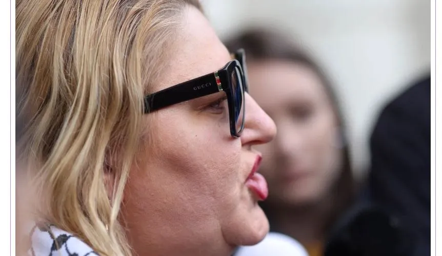 O femeie cu părul blond și ochelari de soare negri este surprinsă în profil.