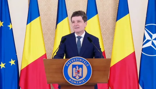 Un bărbat cu costum închis și cravată stă în spatele unui podium de lemn marcat cu un emblema circulară, în fața mai multor steaguri.