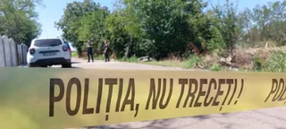 O bandă galbenă cu textul scris pe ea este întinsă în prim-plan, în fața unui drum, unui autoturism alb și a unor copaci verzi.