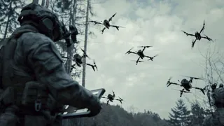 Un soldat în uniformă ține un dispozitiv electronic, privind spre mai multe drone care zboară pe un cer înzăpezit deasupra unei păduri.