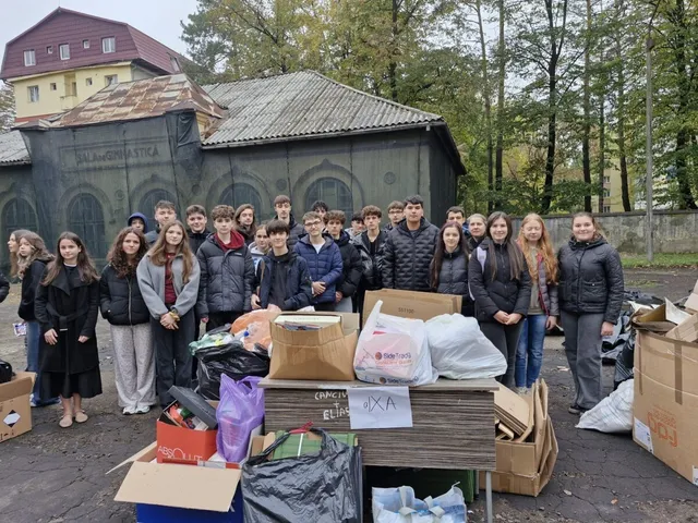 Un grup de elevi în picioare în spatele unei cantități mari de cutii de carton, saci de gunoi și deșeuri reciclabile colectate.