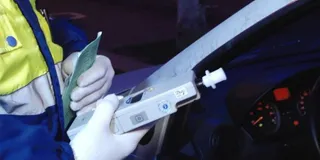 O persoană purtând o vestă reflectorizantă ține un aparat de testare al alcoolului în interiorul unui autovehicul.