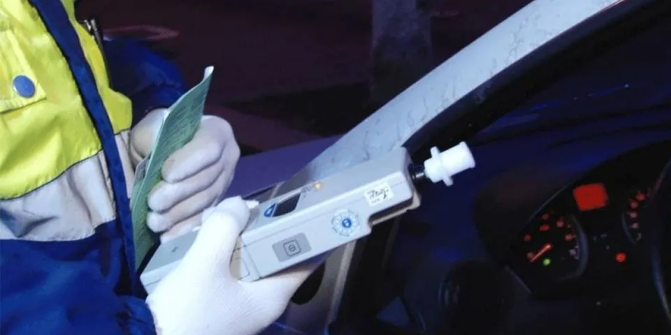 O persoană purtând o vestă reflectorizantă ține un aparat de testare al alcoolului în interiorul unui autovehicul.