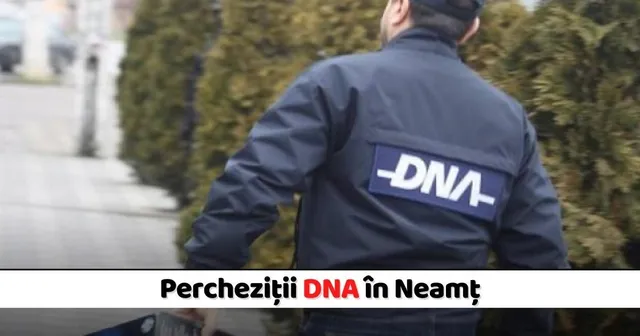 Un bărbat de spate poartă o jachetă albastră cu inscripția DNA pe spate, stând lângă un gard de vegetație deasă.