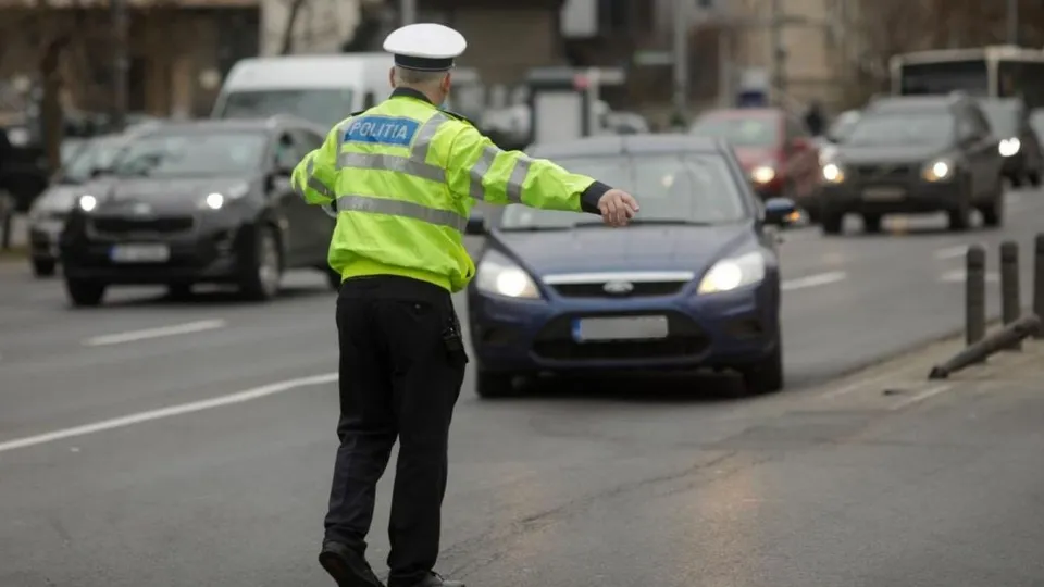 Un polițist cu vestă reflectorizantă verde și cascadă albă stă pe un drum cu mai multe mașini în fundal.