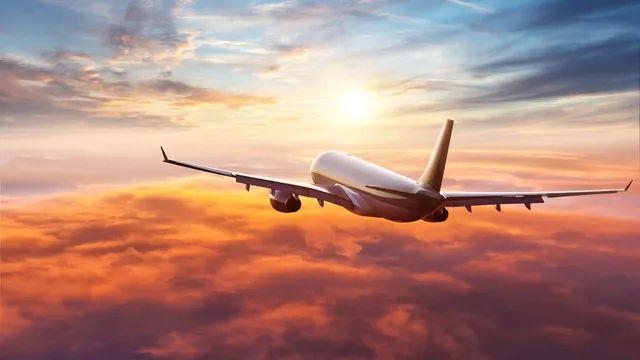 Un avion de pasageri zboară deasupra unui strat de nori sub un cer la apus.