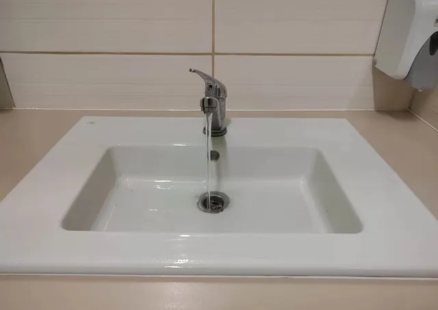 Un robinet de culoare argintie lasă să curgă un jet de apă într-o chiuvetă albă de ceramică.