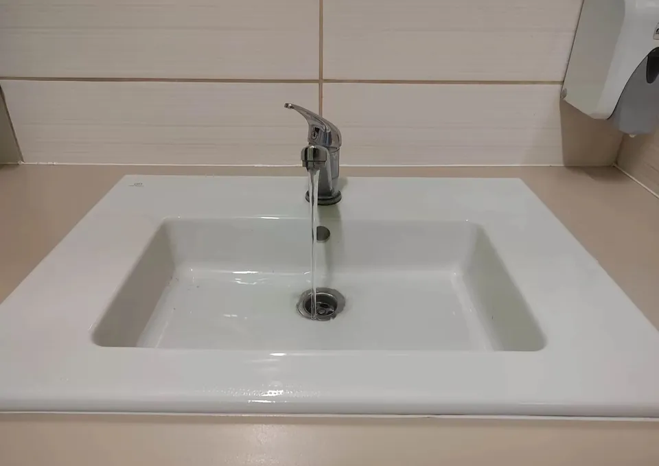 Un robinet de culoare argintie lasă să curgă un jet de apă într-o chiuvetă albă de ceramică.
