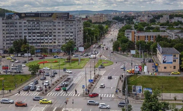 O vedere de sus asupra unei intersecții urbane cu mașini, autobuze, treceri de pietoni și clădiri înalte sub un cer înnorat.