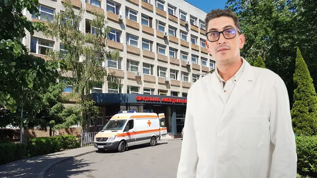 Un bărbat cu ochelari și halat alb stă în prim-plan în fața unei clădiri de spital cu o ambulanță parcată în fața intrării.