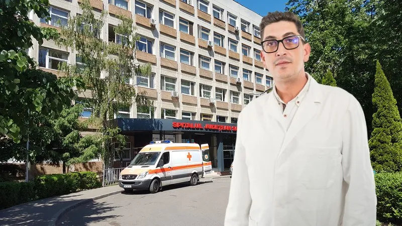Un bărbat cu ochelari și halat alb stă în prim-plan în fața unei clădiri de spital cu o ambulanță parcată în fața intrării.