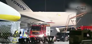 Un avion mare este parcat pe o pistă de noapte lângă un camion de pompieri roșu și un vehicul de serviciu albastru.