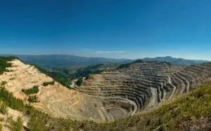 O vedere de la înălțime asupra unei mine a cieloazului cu terase de excavare și versanți de pământ și stâncă sub un cer albastru.