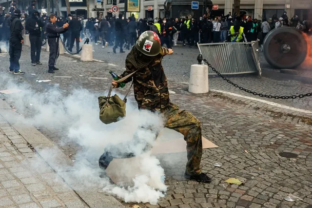 O persoană îmbrăcată în haine de camuflaj și cască aruncă un obiect într-un nor de fum pe un drum pavat.