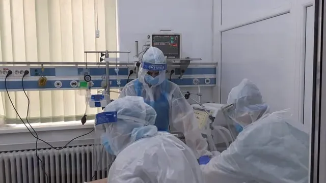 Persoane purtând echipament de protecție alb și măști fac parte dintr-un cadru medical cu echipamente de monitorizare și dispozitive medicale în fundal.